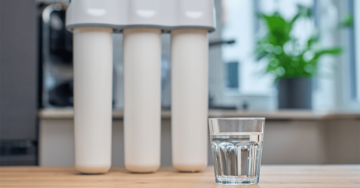 Glass of filtered drinking water and water filtration system on kitchen table