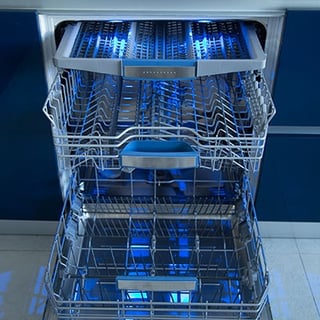 An open dishwasher with blue lighting on a blue background.