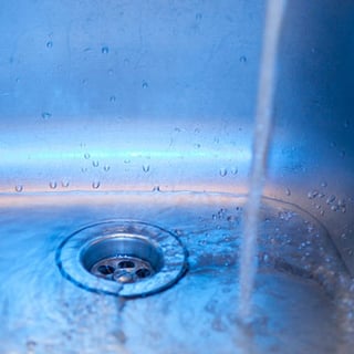 Kitchen sink drain with water pouring into it from the tap above.