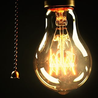 A light bulb with the electrical switch in the on position against a black background.