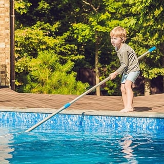 Small boy cleaning a backyard swimming pool.
