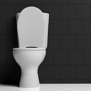 White porcelain toilet in a bathroom with gray subway tiles behind it.