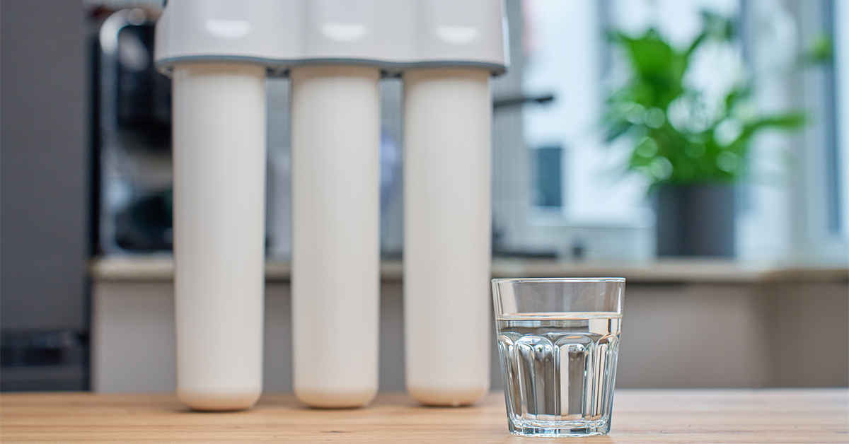 Glass of filtered drinking water and water filtration system on kitchen table
