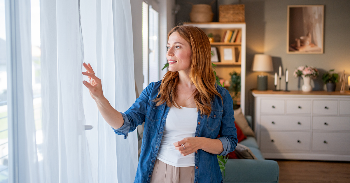 Woman opening curtains at home